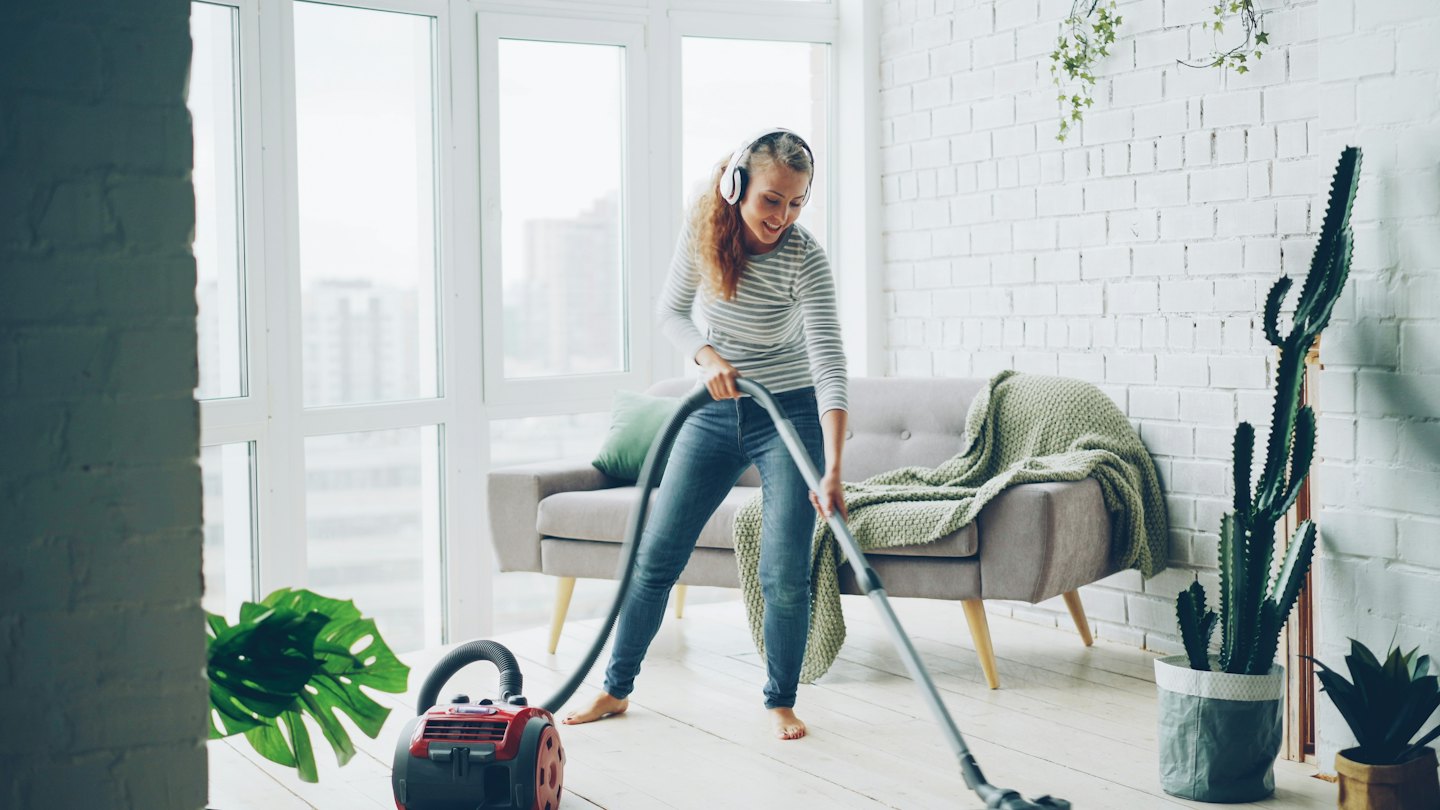 Woman vacuuming the wooden floor of her apartment.